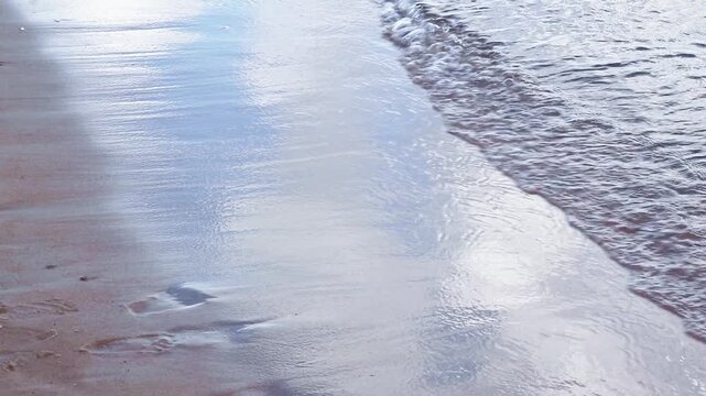Toddler standing barefoot on a sandy beach and splashing in the shallow waves of the sea, creating ripples. Outdoor childhood play, sea ripples, and coastal lifestyle concept