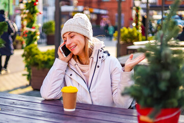 Fototapeta premium Smiling woman enjoying coffee and conversation at an outdoor cafe with winter decor