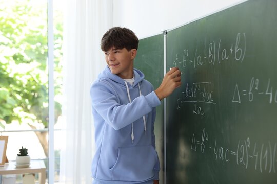 Teenage boy solving equation on chalkboard in classroom