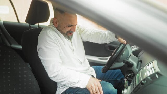 Man gripping steering wheel and reaching to ignition inside parked car on street; frustration vehicle trouble.
