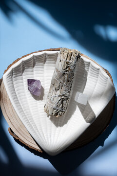 sage smudge stick with amethyst and selenite on shell dish in natural light, concept of cleansing