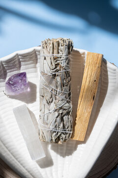 sage bundle with crystals and palo santo on ceramic plate in sunlight creating calming atmosphere