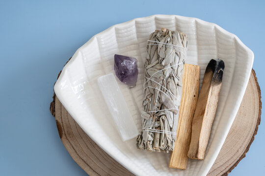 sage smudge stick and palo santo with healing crystals on ceramic plate for spiritual ritual