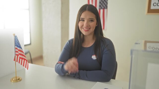 Woman points finger to camera smiling and wearing voted sticker at voting table in building; civic duty pride.