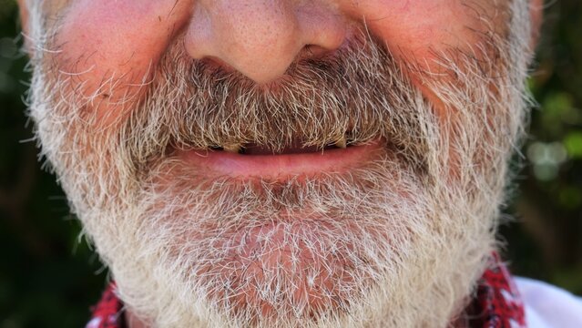 Close up toothless mouth of older bearded man smiling on camera. His expression open and kind, showing the warmth and simplicity of genuine emotion. Scene captures imperfection and human beauty