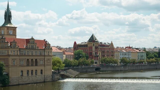 Historic Prague embankment features Smetana Museum tower and a river weir on Vltava. Historic colorful buildings stretch along the waterfront. Perfect for European travel and city tourism.