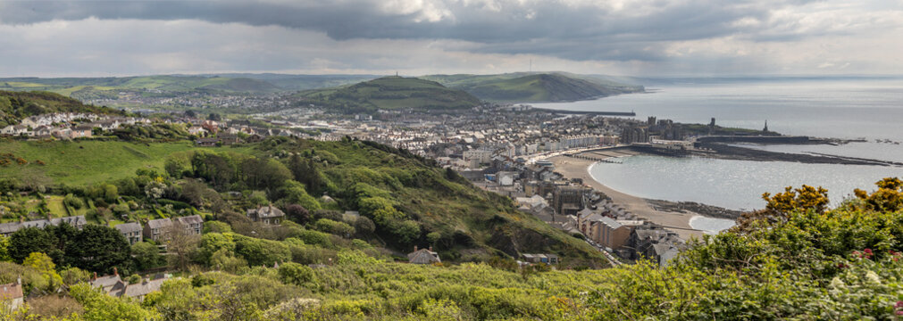 Panoramic View Of A Aberystwyth Coastal Town, Bay and Green Hills Under a Cloudy Sky