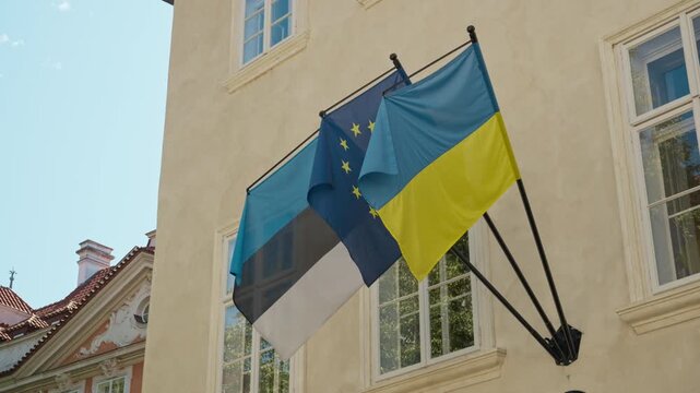 Flags of Estonia, European Union, and Ukraine wave at Estonian Embassy in Prague. Historic building facade stands in Mala Strana district. Concept of European diplomacy, alliance, statehood.