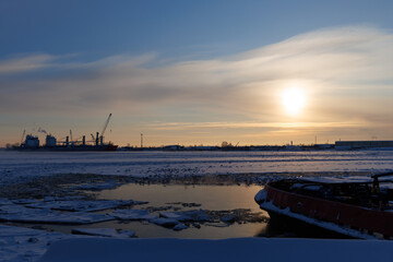 Large cargo vessel locked in frozen river ice with seagulls near open water lane. Winter arctic industrial landscape with copy space. © Konstantin