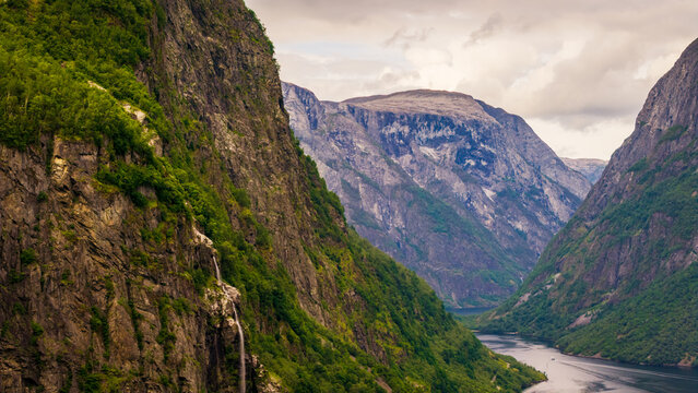 Aerial view of waterfall on the immense mountain walls of Naeroyfjord, revealing layered cliffs, flowing water and the spectacular scale of western Norway's fjord scenery.