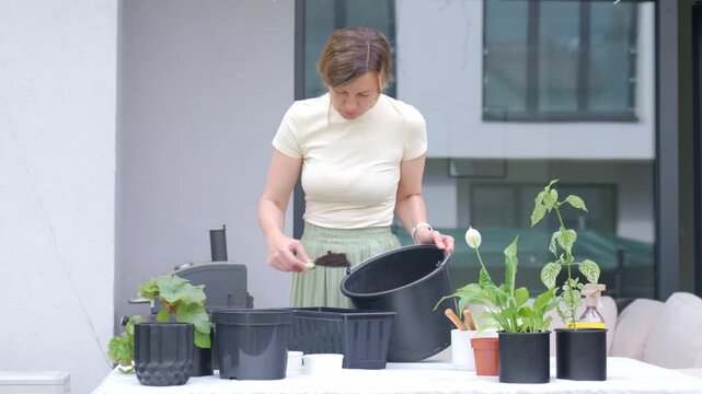 Woman adds dark soil to planter with scoop from black bucket