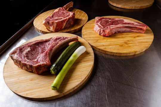 High-quality fresh beef steak cuts like Tomahawk, T-bone and Ribeye uncooked on wooden platters, with fresh ingredients
