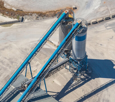 Aerial view of large aggregate storage silos connected by conveyor belt systems at an industrial quarry and crushed stone processing facility, Valence, Auvergne-Rhone-Alpes, France.