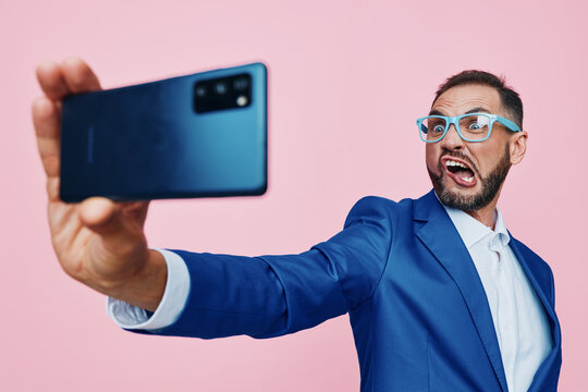 A professional man in a blue suit takes a confident selfie against a vibrant pink backdrop, conveying ambition, style, and a dynamic, forward looking business mood.