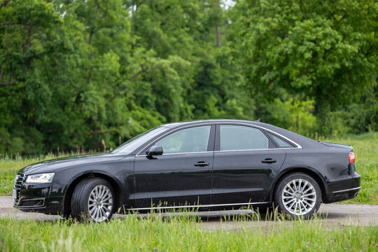 Black Luxury Sedan Parked On Country Road Beside Green Trees After Rainy Drive