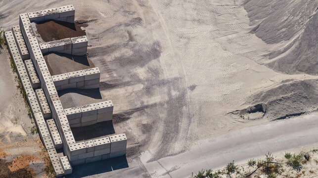 Aerial view of concrete storage bays containing aggregate and bulk material at a mining site, with large stockpiles and heavy machinery tire tracks in Valence, Auvergne-Rhone-Alpes, France.