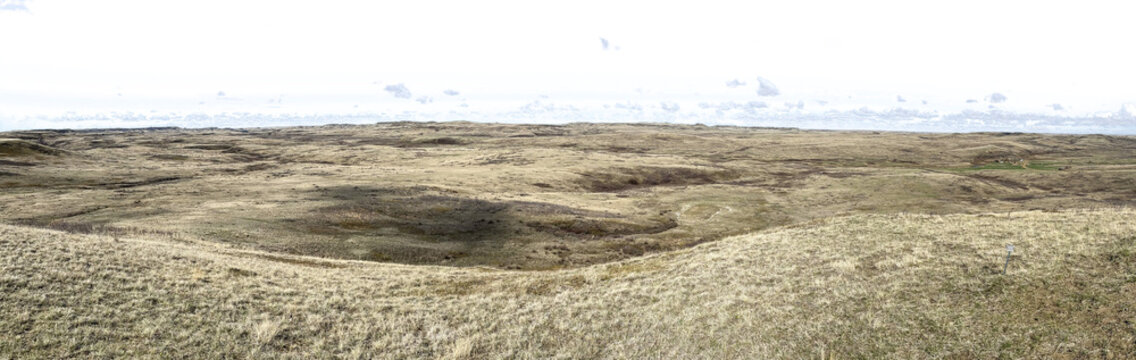 Panorama of pale dry grass in a prairie badlands setting with a transparent sky
