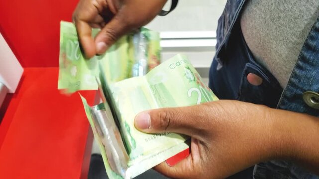 Close up of hands counting a stack of green Canadian twenty dollar bills at an ATM