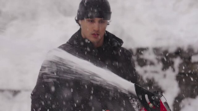 Young man using a snow blower during a heavy snowfall