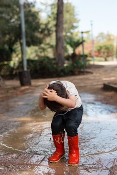 Young boy splashing in a muddy puddle wearing red boots