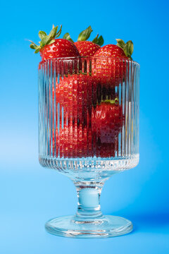 Close-up of fresh whole strawberries with green stems in a fluted glass dessert cup against a sky blue gradient background
