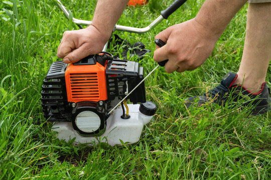 In a grassy area, a person pulls the starter cord of a small engine attached to a lawn mower. The sun is out and the grass is lush. The task is to start mowing the lawn