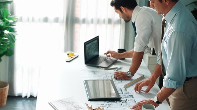 Top view of manager talk and discussing about house construction while sit and write at blueprint at meeting table with project plan laptop displayed house construction and equipment. Alimentation.
