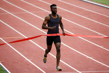 Obraz premium African american male athlete crossing the finish line on a red track, achievement and success in sports, the runner demonstrates determination and focus during the competition