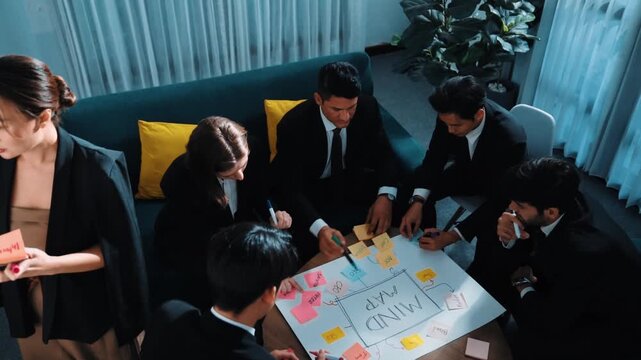 Top view of businesswoman write marketing idea on stick notes while standing near group of diverse people brainstorm financial strategy by using mind map. Start up team working together. Directorate.