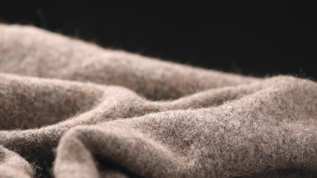 Wool knitted on black background. Real natural beige color wool mohair clothes texture closeup. Craft Cashmere Soft and fluffy merino wool macro shot. Woolen fabric rotating backdrop. 