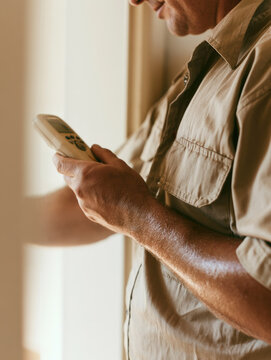 Pest control technician inspection moisture meter wall uniform torso forearm checking device against indoor wall under warm daylight with cropped face and soft background