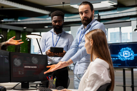 Anxious software development team analyzes a hacker warning popup and plans countermeasures, responding to a data breach alert on screen during an office incident response at a technology startup.