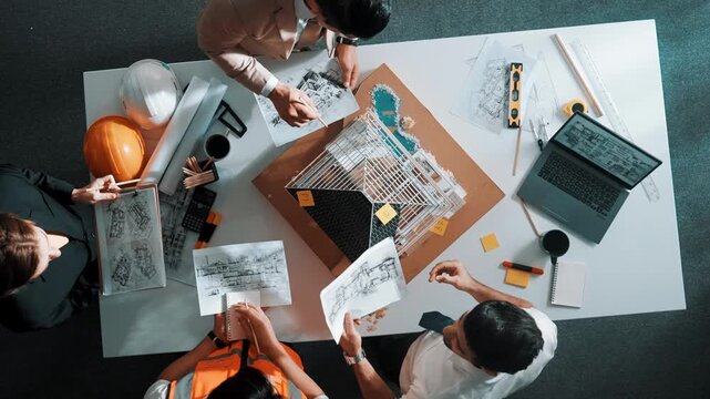 Top view of manager handed blueprint to professional engineer team at meeting table with house model and project plan. Group of architect discussing about design while receive document. Alimentation.
