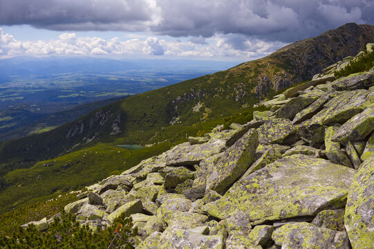 Epic alpine landscape with lichen-covered rocks in foreground, a tarn, and deep valley in the High Tatra Mountains.