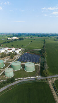 Aerial view of the Sigemi Srl industrial facility featuring large storage tanks and a solar panel array surrounded by green agricultural fields in Lacchiarella, Lombardia, Italy.