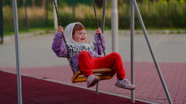 Child enjoying a swing at an outdoor playground, gripping the chains and moving through a playful moment of childhood recreation