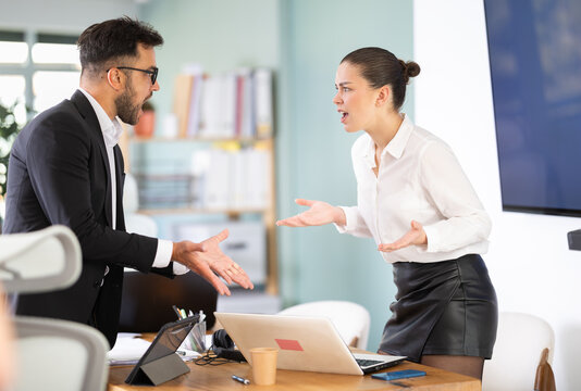 Office employees stand near table and actively argue with each other, they are angry at the inconsistent budget and the wrong project deadlines. Man and woman arguing in the middle of the office
