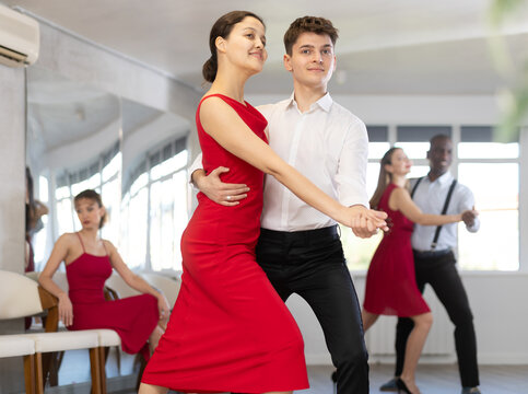 Pretty young woman dancing waltz with partner at group of multinational people in modern ballroom dancing class