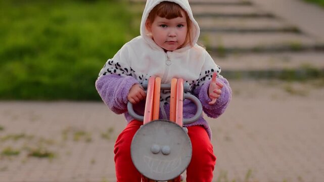 Child playing on a spring rocker in a park, moving from seated riding to standing while enjoying outdoor playground activity