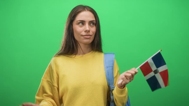 Young woman student with backpack points finger while holding dominican flag in studio; pride celebration joy.