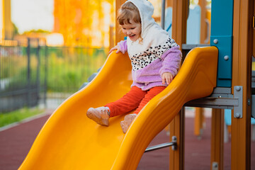 Happy little girl sliding down a playground slide at an outdoor park. Childhood fun, active play, recreation, and joyful summer adventure concept. © Anton Dios