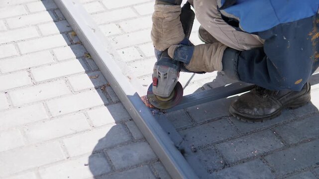 A person is climbing a metal ladder on a paved concrete surface in an outdoor setting, viewed from the side. The scene conveys a neutral mood and is relevant to construction safety and work.