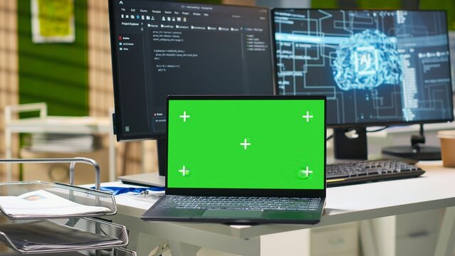 Green screen laptop and computer monitors display AI algorithms in an empty startup workspace, combining a mockup notebook with machine learning deployment and coding tools for software testing.