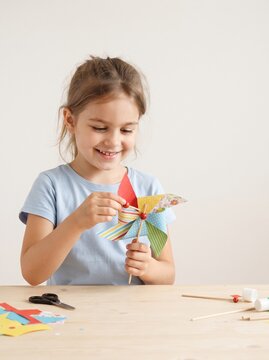Smiling girl making colorful paper pinwheel as creative craft hobby