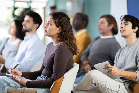 Woman listens attentively to teacher and takes notes in notebook during a professional development course
