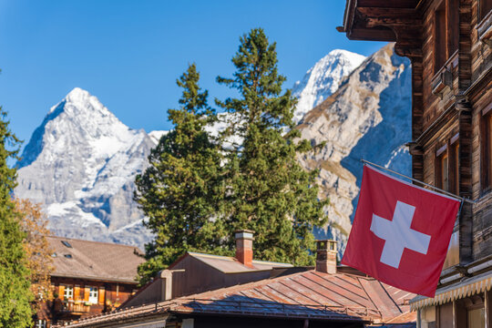 Murren village street detail with traditional wooden chalet, Swiss flag and snow-capped Alps. Murren, Canton of Bern, Switzerland
