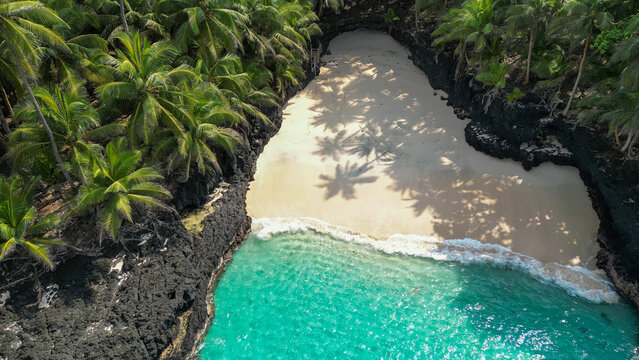 Aerial view of Praia Bateria on Ilh&eacute;u das Rolas, S&atilde;o Tom&eacute;, showcasing a secluded white sand beach bordered by black volcanic rocks, crystal clear turquoise waters, and lush coconut palms.Africa