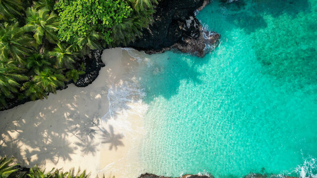 Aerial view of Praia Bateria on Ilh&eacute;u das Rolas, S&atilde;o Tom&eacute;, showcasing a secluded white sand beach bordered by black volcanic rocks, crystal clear turquoise waters, and lush coconut palms.Africa
