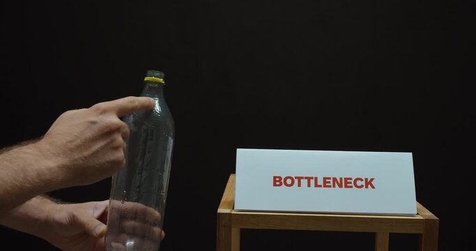Hand holding a plastic bottle beside a &ldquo;Bottleneck&rdquo; sign, illustrating production constraints, workflow delays, limited capacity and process inefficiency.
