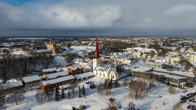 Aerial view of Rakvere Castle and the Church of the Holy Trinity surrounded by snow-covered rooftops and trees in winter in Rakvere, Laane-Viru County, Estonia.